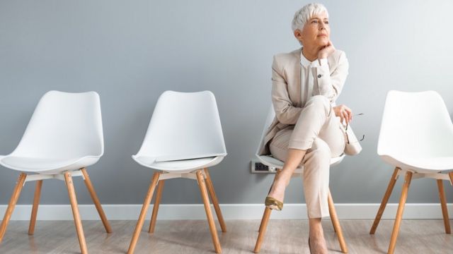 Mulher idosa de cabelos brancos sentada em cadeira branca