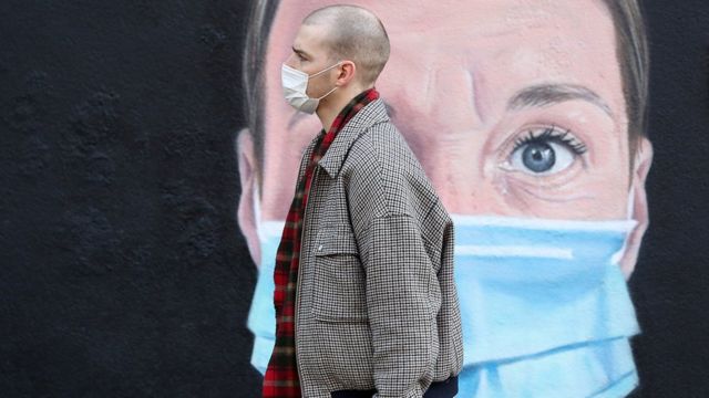 A person wearing a face mask walks past a mural of a nurse in Manchester