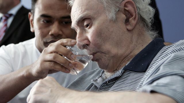 Una ayudante da agua para beber a un hombre de edad avanzada