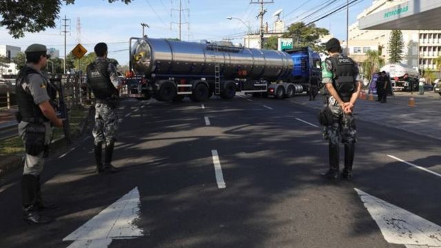 Policiais armados acompanham a chegada de caminhões de combustível em um posto de gasolina