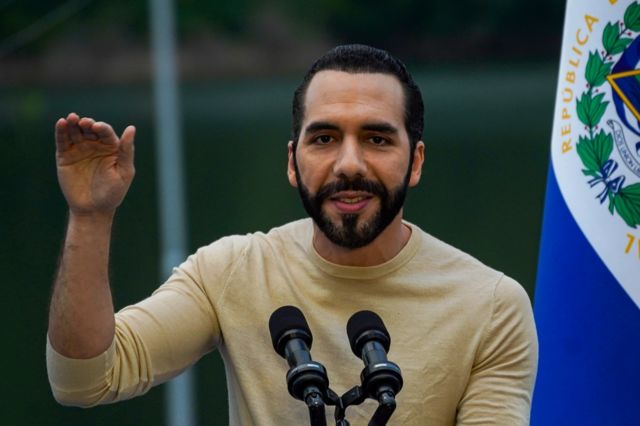 Nayib Bukele gesticula al lado de la bandera de El Salvador