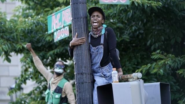 A demonstrator hangs onto a sign pole across from Lafayette Park during a peaceful protest against police brutality in Washington