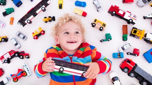 Un niño en medio de un montón de carritos y camiones de juguete