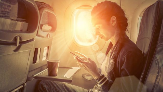 Una mujer, sentada en un avión al lado de la ventanilla por donde entra el sol.
