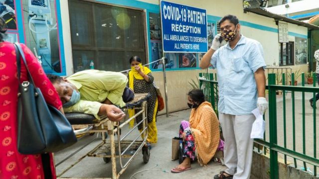Nesta foto tirada em 23 de abril de 2021, parentes esperam ao lado de um paciente com coronavírus deitado em uma maca em um complexo hospitalar para internação em Nova Delhi