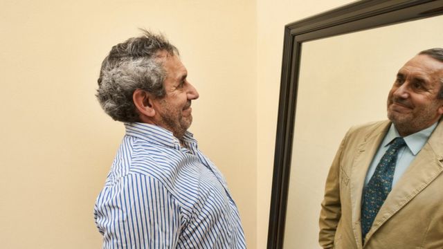 Un hombre mira su reflejko en un espejo, el cual es radicalmente opuesto a la realidad