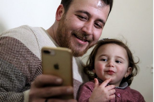 Syrian father Abdullah Mohammed checks a phone with his three-year-old daughter Salwa at their home in Sarmada, a town in Syria's last rebel pocket in the Idlib province, 19 February