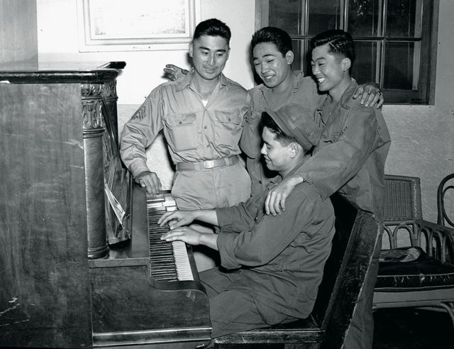 A soldier plays an piano as soldiers sing along