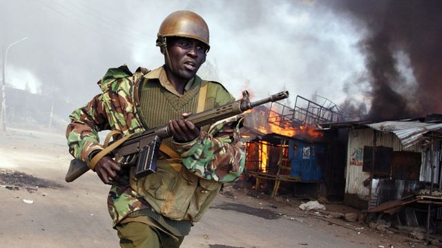 Umupolisi wa Kenya yirukanka iruhande rw'inzu zirimo gushya zari zatwitswe n'abashyigikiye umukandida perezida Raila Odinga, mu gace gatuwemo mu bucucike ka Mathare k'i Nairobi, ku itariki ya 30 y'ukwezi kwa cumi na kabiri mu 2007