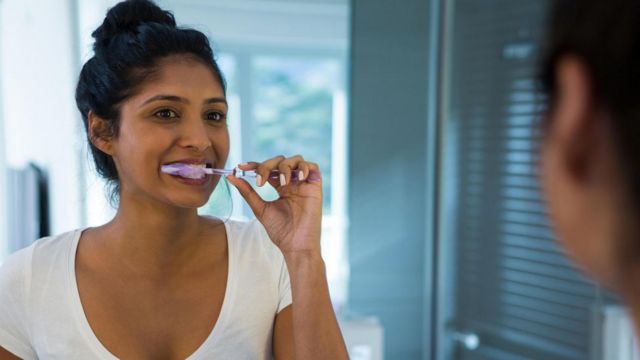 Mulher escovando dente em frente a espelho