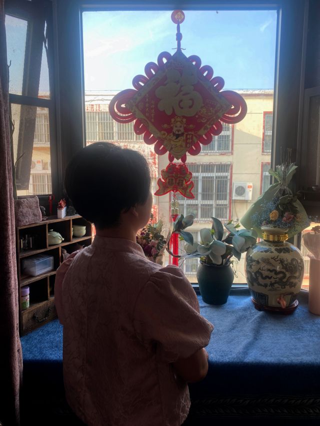 Chinese woman Zhang Ming looks out the window of her house.