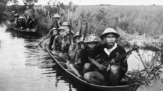 Sur l'eau, deux pirogues. A bord, des soldats vietcongs armés de fusils.