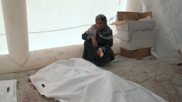 A woman sits next to the bodies of some of her relatives killed in an Israeli bombardment