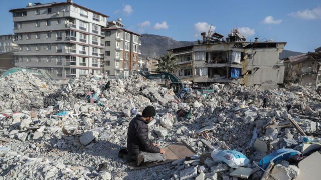 depremde yıkılmış bina üzerinde namaz kılan erkek