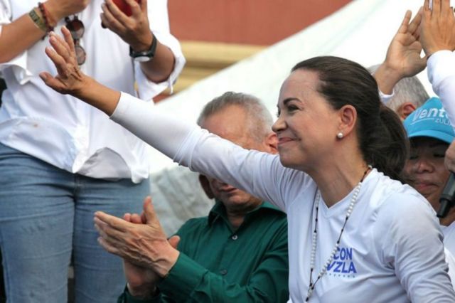 María Corina Machado  sorrindo enquanto acena para pessoas em comício