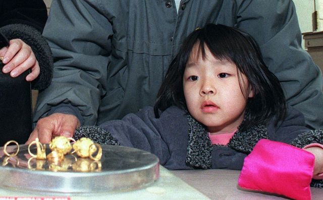 Una niña surcoreana observa a su padre pesar unos anillos de oro que está donando al país