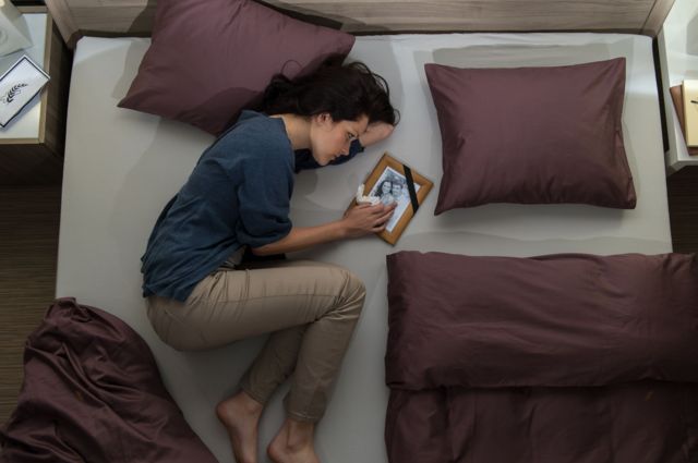 Una mujer pasa su duelo en cama mientras sostiene un retrato.