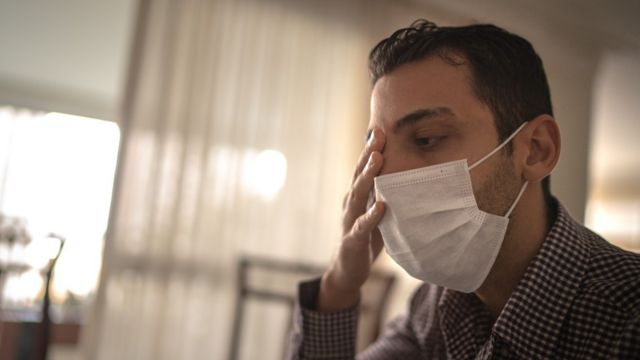 Hombre con mascarillas frotándose un ojo