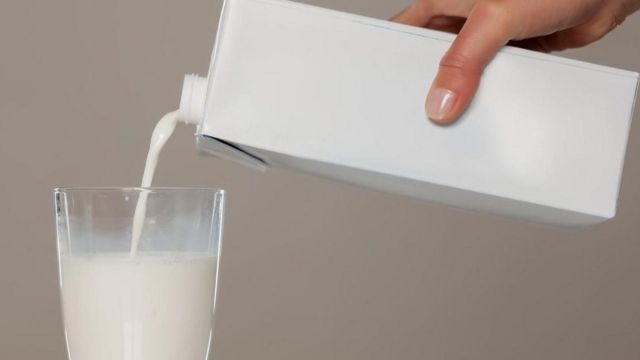 Una persona llenando un vaso de leche de larga duración