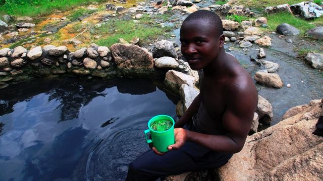 Un jeune homme Bakonzo est photographié avec une boisson médicinale à la source chaude d'Embugha (Rwagimba).