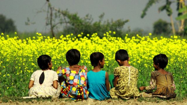 একটি সর্ষে খেতের পাশে শিশুরা।