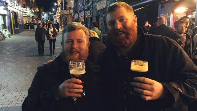 Two men who look very similar drinking pints of beer together.