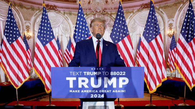 Fotografia colorida mostra Trump, um homem branco e idoso em frente um púlpito