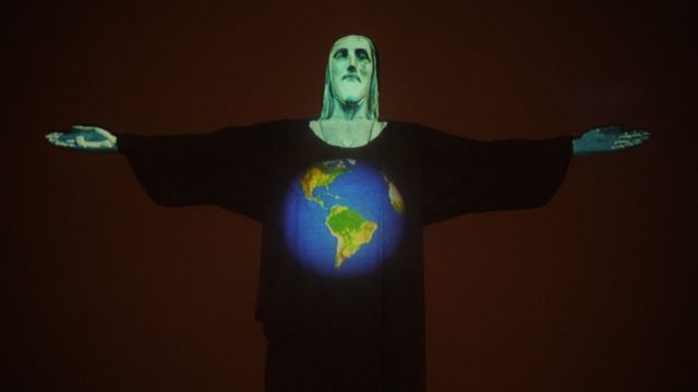 Estátua do Cristo Redentor à noite, iluminada por projeção mostrando um desenho do planeta em homenagem a vítimas da covid-19