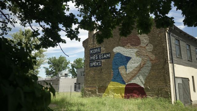 Mural showing solidarity to Ukraine shows two women hugging, in Ukrainian and Latvian colours