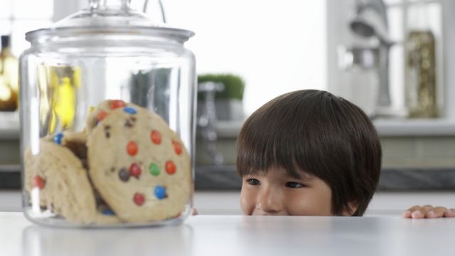 Imagem mostra menino observando pote de biscoitos