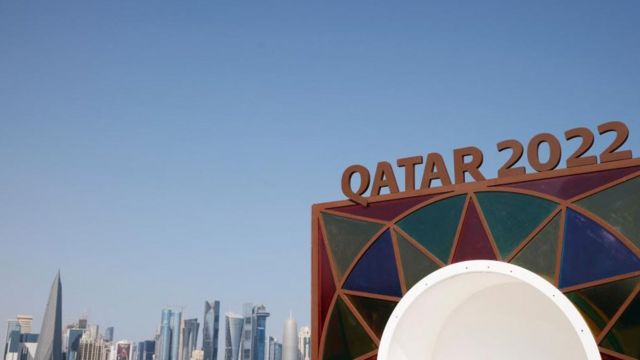 Logo Piala Dunia dengan gedung pencakar langit Doha di latar belakang.
