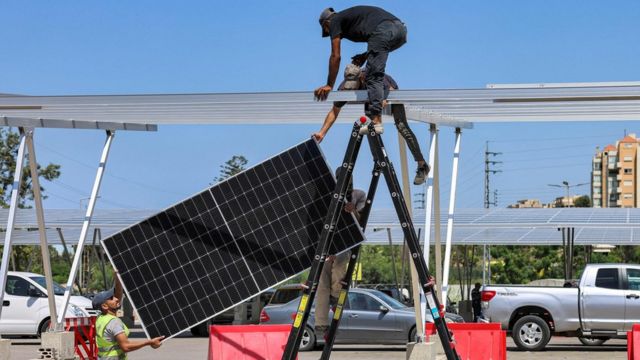 Workers install new solar panels as shades on vehicles in the parking lot of a shopping mall in the northern Lebanese city of Byblos on August 26, 2022.