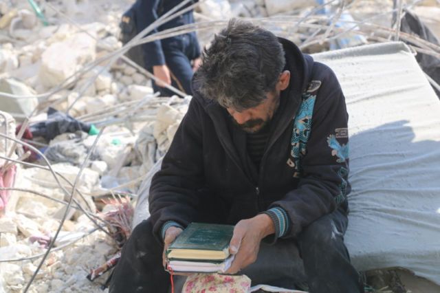 Мужчина на обломках своего дома в городе Алеппо с кораном в руках