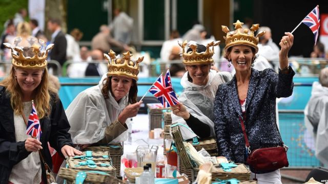 Women don royal crowns while waving British flags at their picnic
