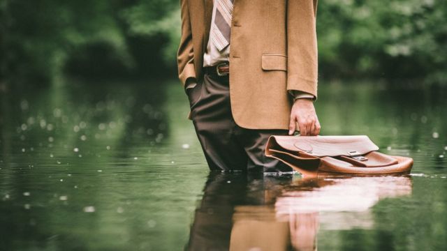 Homem de terno, gravata e maleta em meio a um lago