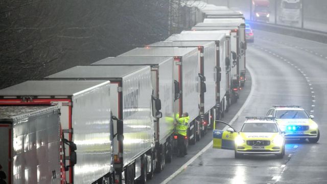 Police officers speak to a driver in one of lorries parked on the M20 motorway after France closed its border