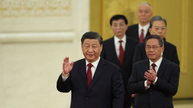 Anggota Komite Tetap Politbiro biasanya diurutkan berdasarkan urutan.  Dalam foto tersebut, Li Qiang muncul tepat di belakang Xi Jinping.