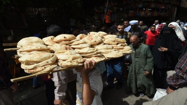 رجل يحمل فوق رأسه خبزا في شارع مزدحم