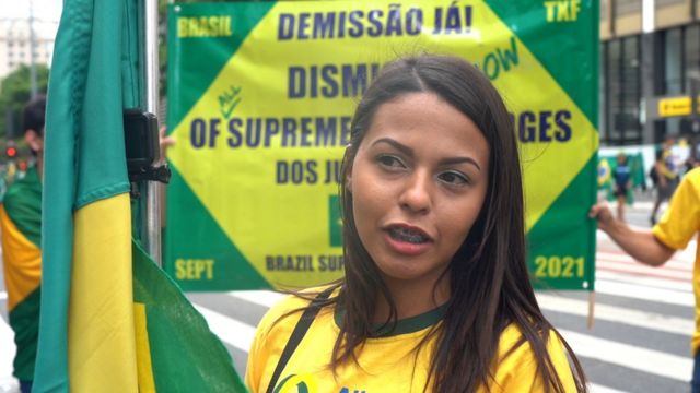 Maiara Moura fala, com grande cartaz verde amarelo atrás