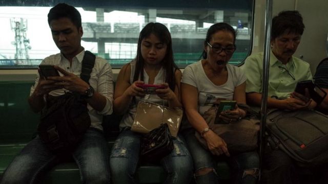 Filipinos pegados a sus celulares en un tren en Manila