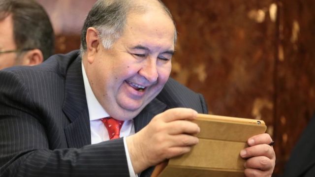 Алишер Усманов смеется, гляд в планшет