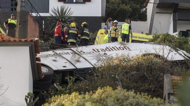 Equipes de emergência trabalham perto de ônibus caído em meio a casas