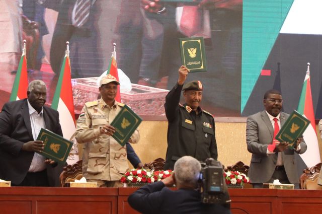 قائد الجيش السوداني عبد الفتاح البرهان وقائد قوات الدعم السريع محمد حمدان دقلو يرافقه قادة الجماعات المدنية يرفعون وثائق موقعة لاتفاق إطاري لإنهاء الجمود السياسي في الخرطوم