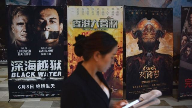 A woman looks at her mobile phone near movie posters outside a theatre in Beijing on May 23, 2018.