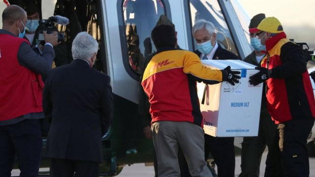 El presidente chileno Sebastián Piñera (centro derecha) observa a los trabajadores transportar el primer lote de la vacuna Pfizer-BioNTech a un helicóptero en el aeropuerto de Santiago.  Foto: 24 de diciembre de 2020