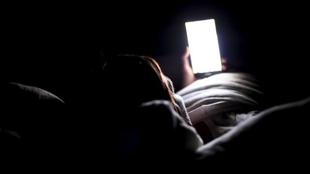 Una persona mirando el celular en la cama