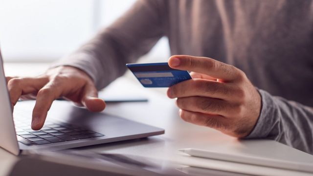 Homem na frente do computador com cartão de crédito