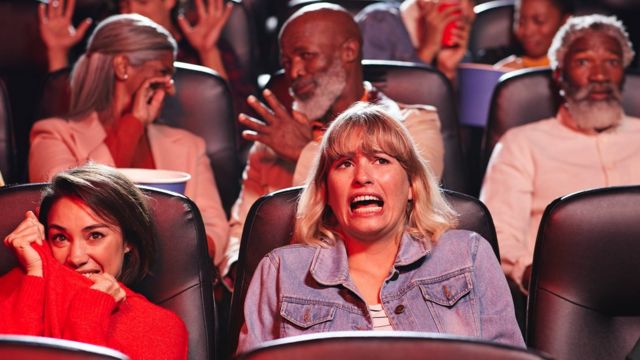 The audience reacts to a horror movie in the cinema.