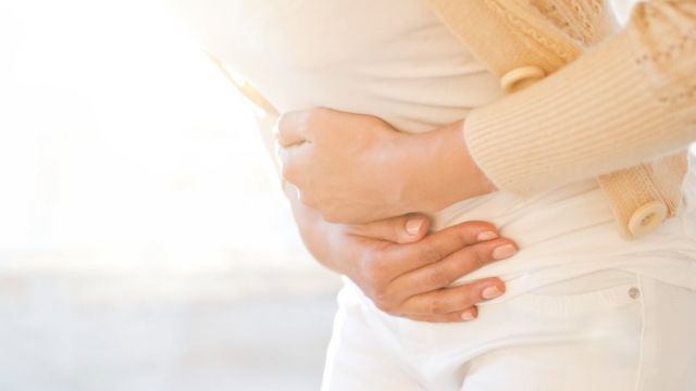 Mujer con las manos sobre su abdomen en gesto de dolor