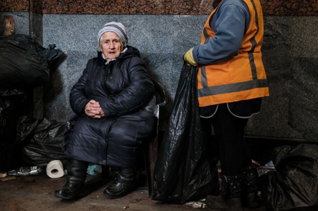 Uma idosa de 91 anos e roupas de frio sentada em uma cadeira